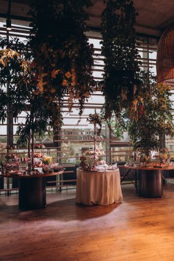 Lokantada şekerli büfe masası. Çiçeklerle süslenmiş bir yüzeyde kekler, pastalar, gurme şekerlemeler. 