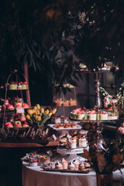 Lokantada şekerli büfe masası. Çiçeklerle süslenmiş bir yüzeyde kekler, pastalar, gurme şekerlemeler. 