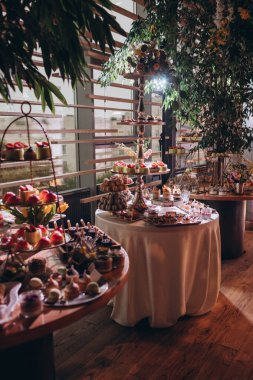 Lokantada şekerli büfe masası. Çiçeklerle süslenmiş bir yüzeyde kekler, pastalar, gurme şekerlemeler. 