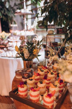 Lokantada şekerli büfe masası. Çiçeklerle süslenmiş bir yüzeyde kekler, pastalar, gurme şekerlemeler. 