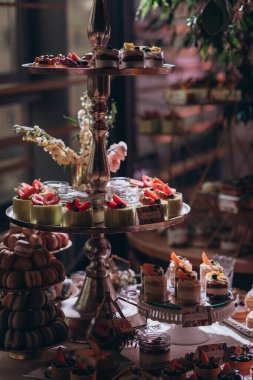 Lokantada şekerli büfe masası. Çiçeklerle süslenmiş bir yüzeyde kekler, pastalar, gurme şekerlemeler. 