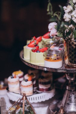 Lokantada şekerli büfe masası. Çiçeklerle süslenmiş bir yüzeyde kekler, pastalar, gurme şekerlemeler. 