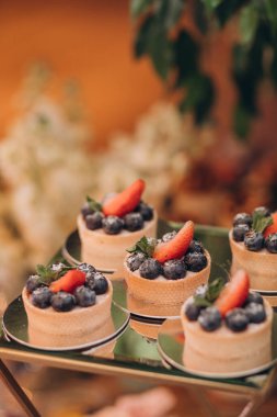 Lokantada şekerli büfe masası. Çiçeklerle süslenmiş bir yüzeyde kekler, pastalar, gurme şekerlemeler. 