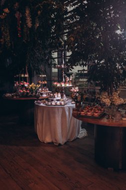 Lokantada şekerli büfe masası. Çiçeklerle süslenmiş bir yüzeyde kekler, pastalar, gurme şekerlemeler. 