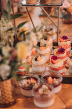 Lokantada şekerli büfe masası. Çiçeklerle süslenmiş bir yüzeyde kekler, pastalar, gurme şekerlemeler. 
