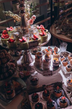 Lokantada şekerli büfe masası. Çiçeklerle süslenmiş bir yüzeyde kekler, pastalar, gurme şekerlemeler. 