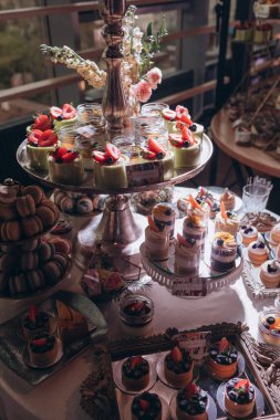 Lokantada şekerli büfe masası. Çiçeklerle süslenmiş bir yüzeyde kekler, pastalar, gurme şekerlemeler. 