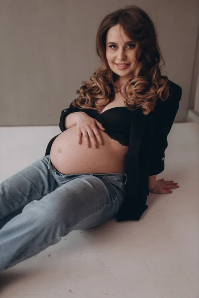 奢华的怀孕妇女端坐在坚实的背景上 露出她的腹部 — 图库照片