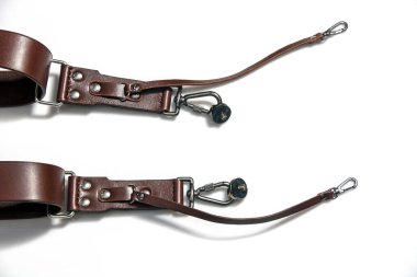 Kahverengi el, beyaz arka planda izole edilmiş nikel metal elementlerle doğal deri fotoğraf makinesi askısı parçası yapmış. İki cihaz için fotoğraf ekipmanı, stil, eski moda, eski moda