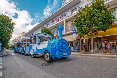 Tossa de Mar, Girona, İspanya - 29 Temmuz 2019: Eski İspanyol kasabasının asfalt yolunda mavi turist lokomotifinin geniş açılı görüşü