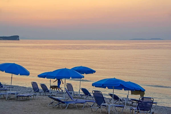 Sombrillas Azules Tumbonas Playa Atardecer Iluminadas Por Retroiluminación Naranja Mujer —  Fotos de Stock