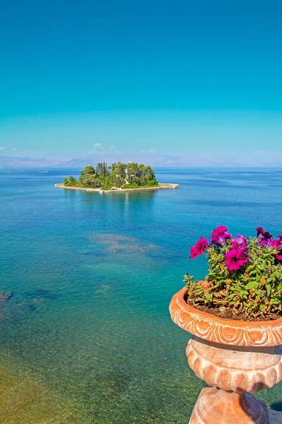 在希腊科孚蔚蓝的大海中 一个色彩艳丽的垂直风景 粉红的花朵在粘土盆里 与绿色的小岛庞蒂科尼西相映成趣 背景模糊 — 图库照片