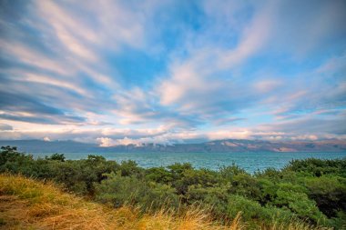 Beautiful landscape with colorful dramatic sunset clouds over the Sevan lake in Armenia with green bushes on foreground. Wide angle view