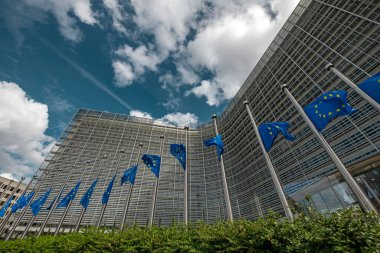 Avrupa Birliği 'nin mavi bayraklı kule kuyruğunun, Belçika, Brüksel' de dramatik bir gökyüzü altında Avrupa Komisyonu binasının arka planına göre düşük açılı görünümü. AB bayrak sembolü