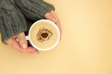 Sıcak süveter giymiş bir kadının elleri bir fincan kahve tutuyor, boşluğu kopyalıyor..