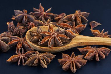 Star anise on a wooden spoon on a dark background, close-up.
