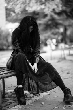 Bankta oturan bir kadının dramatik siyah beyaz görüntüsü.