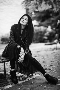 Parktaki bankta poz veren genç kadın, siyah ve beyaz.