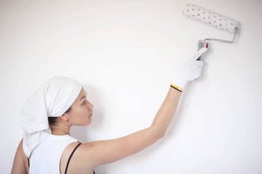 Yükselmiş elleriyle duvarı silindirle boyayan genç bir kadın.