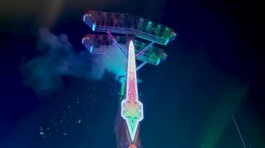 lights at night and large extreme funfair carousel in motion with passengers on board