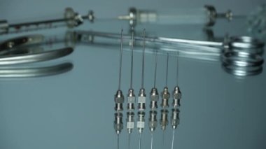 old metal needles from a syringe for injection against the background of medical instruments on a mirror surface. Pan right. Video. The background is out of focus.