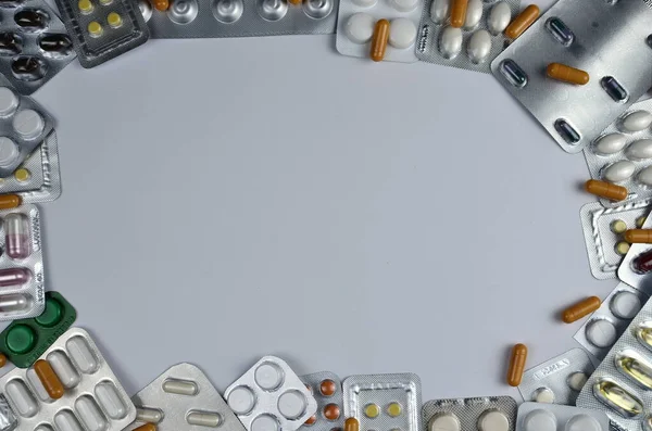 a variety of medical pills in blister packs are laid out in the form of a frame on a gray background. Photo