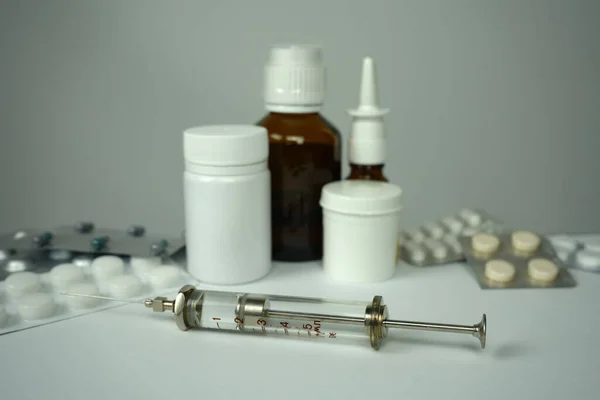 a glass medical syringe on a white surface against the background of jars and blisters with medicines. Blurred background. A photo.