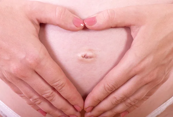 Mulher segurando suas mãos em forma de coração em sua barriga grávida — Fotografia de Stock