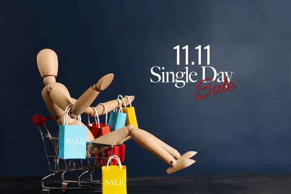 Stock image 11.11 singles day sale concept, shopaholic wooden doll with lots of shopping bags on arm and shopping cart