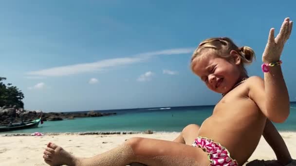 Little girl in pink panties is relaxing on beach. She has ponytails on her  hair, beads on her neck, bracelets on her hands. She gets up and runs with  mother to sea.