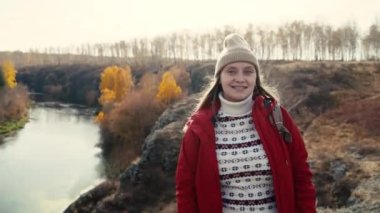 Gülümseyen ve diş teli takan beyaz kadın dişlerinde görünür. Güneşe bakıp gülüyor. Rüzgar saçı geliştirir ve ışıkta parıldarlar. Sonbahar yürüyüşü, doğa, sarı ağaçlar, nehir.