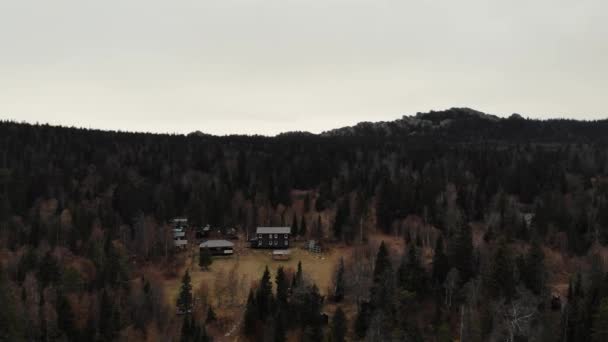 Vista aérea del bosque de coníferas de otoño cerca de la cima de la montaña. Hay pequeñas casas de madera y paneles solares. Pequeños caminos van hacia el bosque. Senderismo, vida lejos de la ciudad — Vídeos de Stock