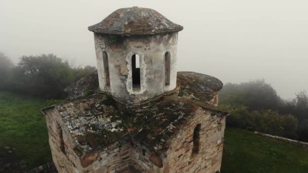 Повітряний вид старовинної християнської церкви Сентінел, Кавказ. Розташований на хребті. Густий туман покриває білі кам'яні стіни церкви і зелень навколо. Дах покритий мохом. — стокове відео