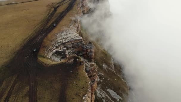 Widok z powietrza kamiennego amfiteatru w gęstych chmurach, płaskowyż Bermamyt, Kaukaz. Lecąc nad majestatycznym urwiskiem, wzdłuż którego biegnie droga po ziemi. Mgła przesuwa się na strome zbocze. region Elbrus — Wideo stockowe