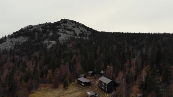 Vista aérea da floresta de coníferas do outono perto do topo da montanha. Existem pequenas casas de madeira e painéis solares. Pequenos caminhos vão para a floresta. Caminhadas, vida longe da cidade — Vídeo de Stock