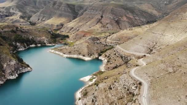 Légi felvétel az azúri Gizhgit hegyi tóról, Kaukázus. Kék víz csillog a napfényben. Felséges hegyvonulat látható. A csúcsok csúcsai ragyognak a felhős égbolton. Drón videofelvételek készítése — Stock videók