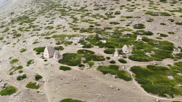 Vista aérea de las criptas de piedra gris de la ciudad de los muertos, Cáucaso. Casas luminosas con techos puntiagudos en pendiente entre vegetación baja y piedras. Antiguo entierro tradicional caucásico — Vídeos de Stock