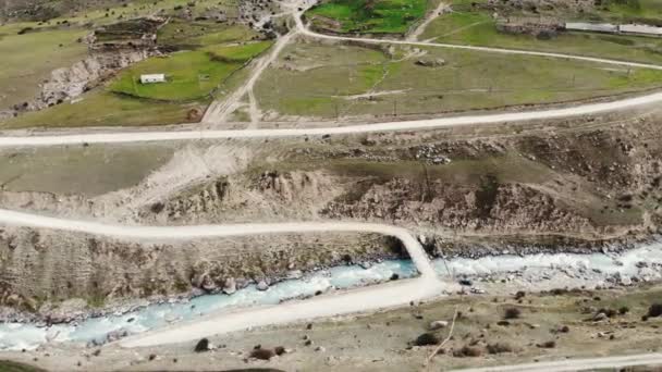 Vista aérea da aldeia localizada entre as montanhas do Cáucaso. Está localizado perto do rio. Picos de montanhas são muito altos e severos. As encostas são cobertas com rochas e pequena vegetação verde — Vídeo de Stock