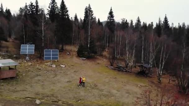 Aerial view of the autumn coniferous forest near the top of the mountain. There are people, small wooden houses and solar panels. Small paths go into the forest. Hiking, life away from the city