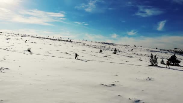Widok z lotu ptaka na zboczu góry, Ural Południowy. Turyści spacerują szlakiem przez zaśnieżoną łąkę na szczyt góry. Jasnoniebieskie niebo pokryte jest małymi jasnymi białymi chmurami. Słoneczko. Wędrówki — Wideo stockowe