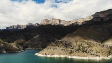 Gök mavisi Gizhgit Gölü, Kafkasya 'nın havadan görünüşü. Mavi su gün ışığında parıldıyor. Yüksek görkemli dağ sırası görülebilir. Bulutlu gökyüzünde sivri tepeler parlıyor. İnsansız hava aracı video çekimleri