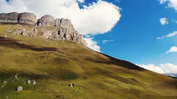 Kuzey Kafkasya 'daki dağ geçidinin hava manzarası. Dağ tepelerinin aralığı parlak güneşi aydınlatır. Yamaçlar yemyeşil ve kayalarla kaplıdır. Bulutların gölgesi çayırlarda koşuyor. — Stok video