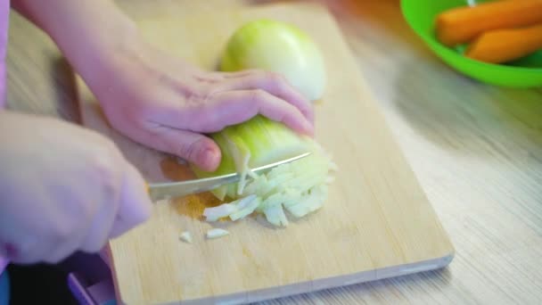 Kobieta drobno kroi młodą cebulę na drewnianej desce ostrym nożem w kuchni do gotowania. Małe kawałki spadają kawałek po kawałku na planszy. Zdrowe jedzenie, warzywa, gotowanie w domu — Wideo stockowe