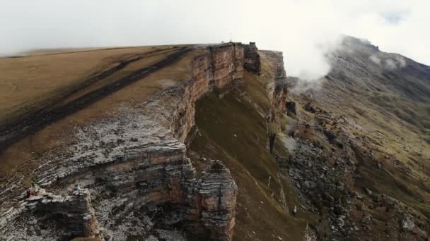 Vista aérea del anfiteatro de piedra en densas nubes, meseta de Bermamyt, Cáucaso. Volando sobre majestuoso acantilado cara a lo largo de la cual el camino corre a lo largo del suelo. La niebla se está moviendo cuesta arriba. Región de Elbrus — Vídeo de stock