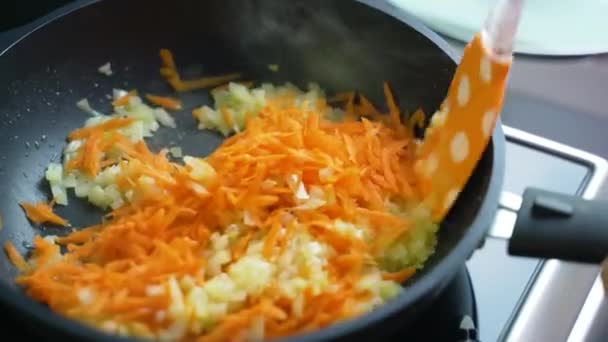 Friggere le cipolle e le carote tritate in olio preriscaldato in padella in cucina a casa. Le fette di cipolla leggera tritata e le carote grattugiate sono mescolate con spatola di silicone. Cucinare a casa, mangiare sano — Video Stock