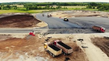 Arabalar için test alanına asfalt döşeyen sarı yol silindirlerinin hava manzarası. Yakınlarda karavanda taze asfalt olan büyük kamyonlar var. Yol yapımı