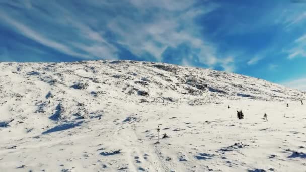 Vista aérea de la ladera de nieve de montaña, Ural Sur. El prado de nieve al pie de la montaña. El cielo azul brillante está cubierto de pequeñas nubes blancas claras. Soleado. Pequeños abetos crecen. Senderismo, turismo — Vídeo de stock