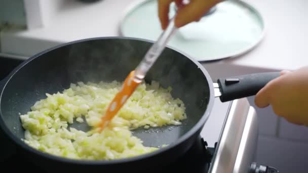 Gehackte Zwiebeln in vorgeheiztem Öl in schwarzer Pfanne in der heimischen Küche braten. Die gehackten Zwiebelscheiben werden mit Silikonspachtel vermischt. Gesunde Ernährung, Gemüse, Kochen zu Hause — Stockvideo