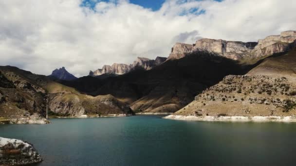 Вид з повітря на зелене гірське озеро Gizhgit, Кавказ. Блакитна вода мерехтить на сонці. Видно величне гірське пасмо. На хмарному небі сяють вершини гір, що здіймаються на гору. Відеобстріл дронів — стокове відео