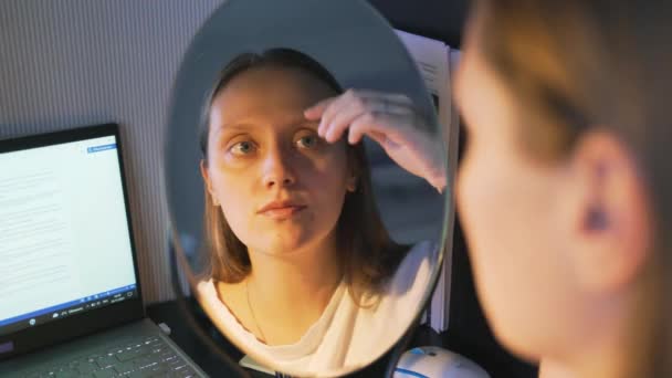 La joven se mira en el espejo, examina la piel de su cara y se molesta. Hay enrojecimiento y granos en la cara. La chica está molesta. Salud, cosmetología — Vídeos de Stock